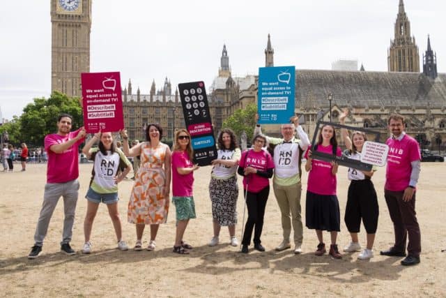 A group of RNID supporters holding placards standing outside the Houses of Parliament