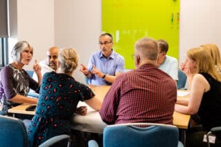 A group of work colleagues seated around a table in an office having a discussion.