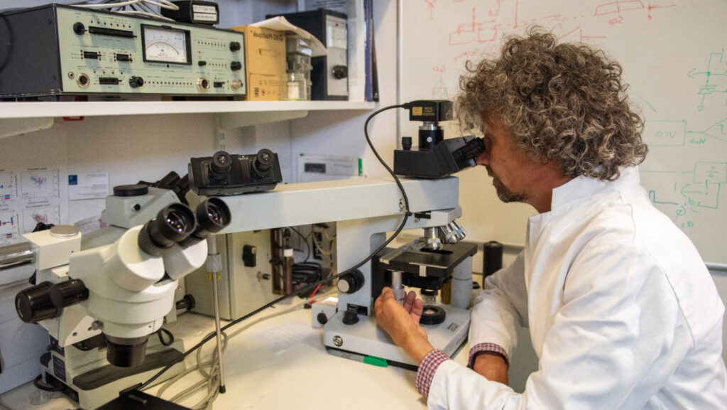 Male scientist sat at desk looking into a large microscope 