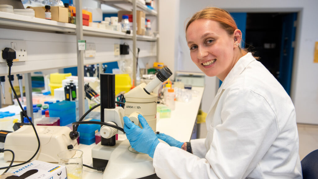 Female scientist with microscope smiling at camera