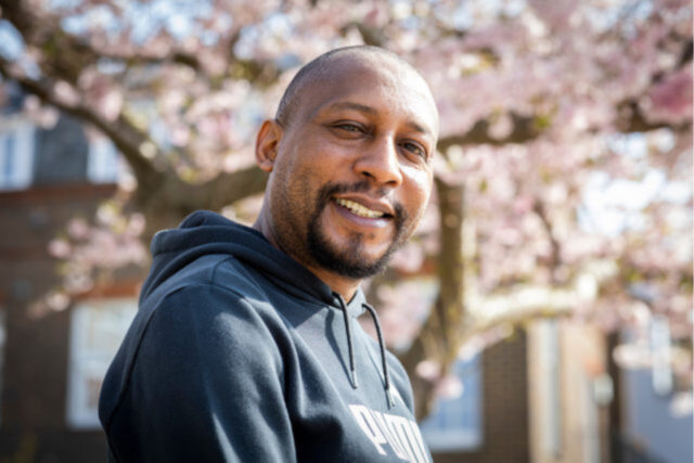 A man standing outside in front of a blossom tree, smiling