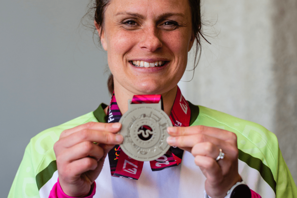 A woman in an RNID running vest, holding a medal up to the camera and smiling. 