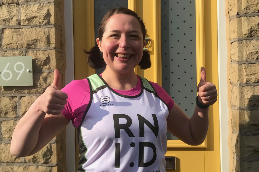 A picture of a woman wearing an RNID running vest and smiling at the camera with her thumbs up.