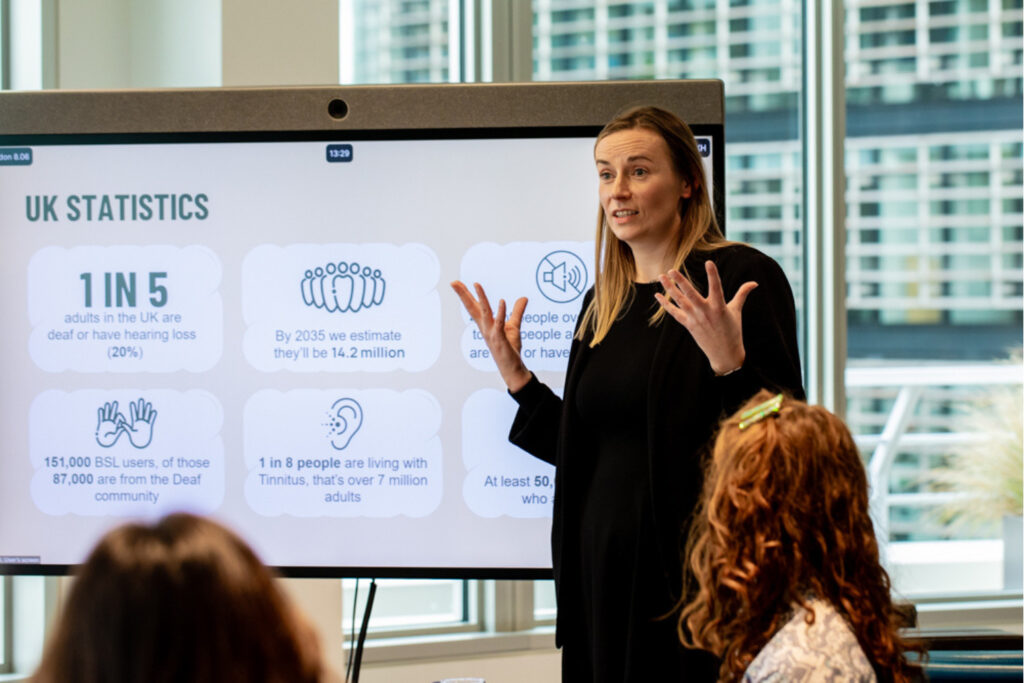 A woman leading a training session by a screen showing statistics