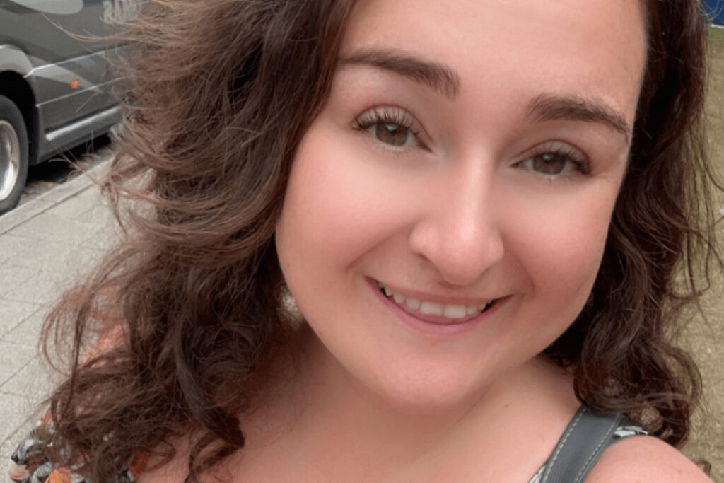 Picture of a woman with brown curly hair smiling outdoors.