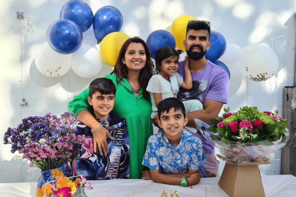 A family portrait at a birthday party. A mother and father smiling with three children, balloons and flowers. 