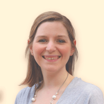 A photograph of a woman with shoulder-length hair, a grey top and a necklace. She's smiling at the camera. 