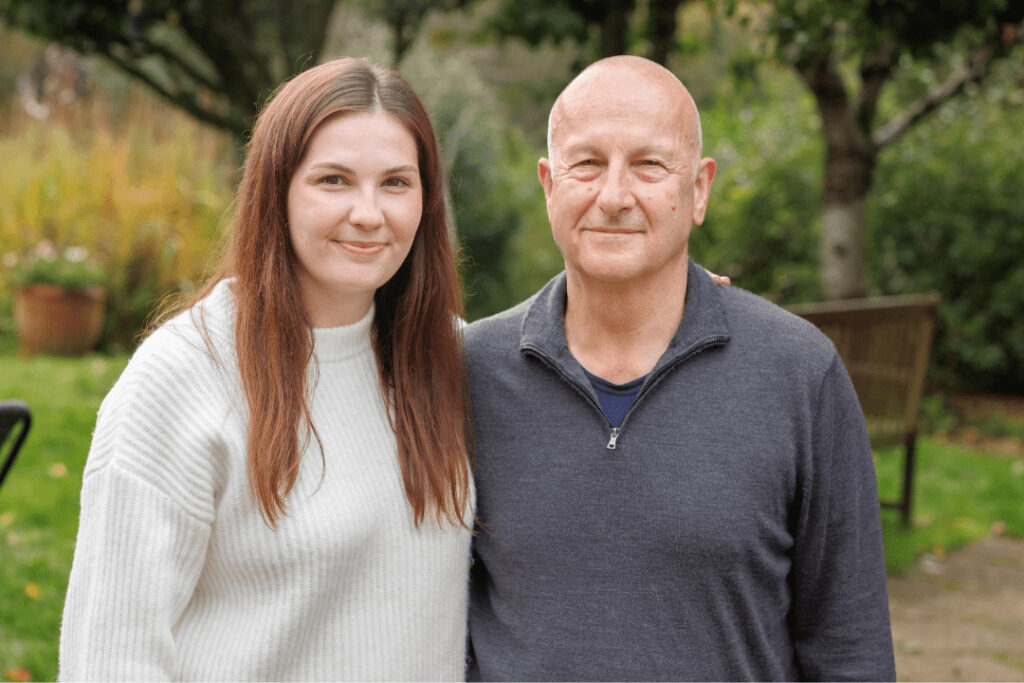 John, an older man, and his daughter, Matilda, smiling and posing for the camera in the garden. 