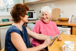 Two women chatting at the kitchen table and looking at a tablet device