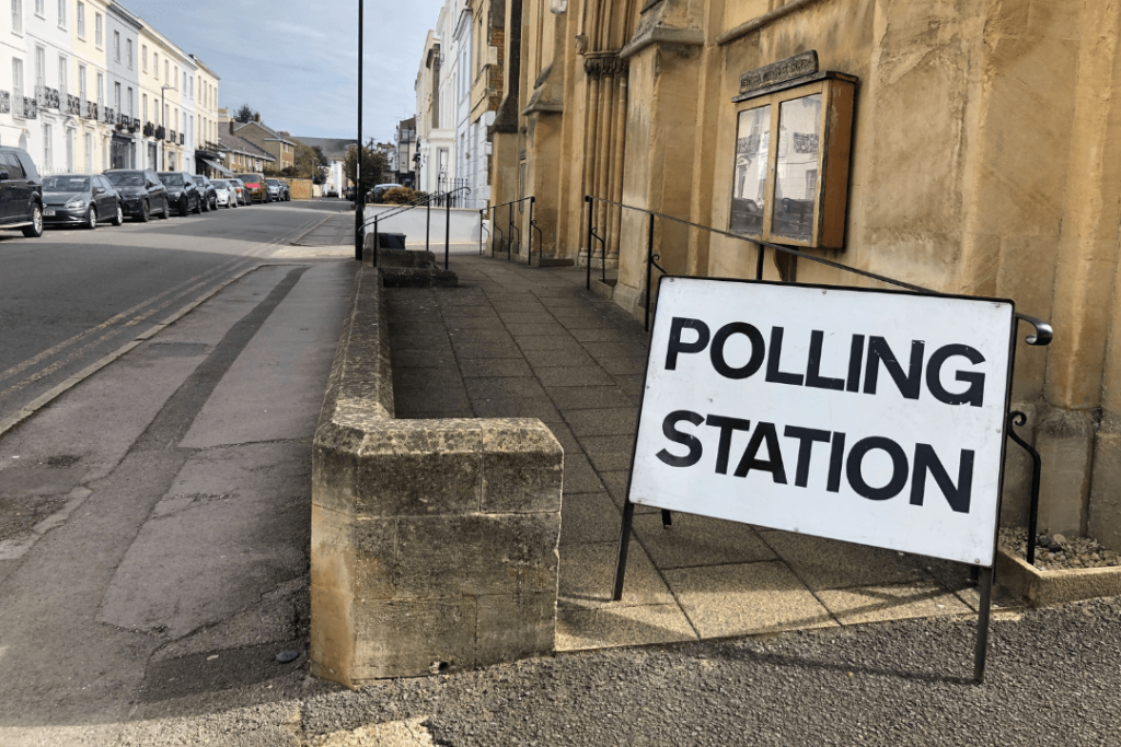 A photograph of a street in the UK with a road sign saying: "POLLING STATION" outside of an old building.