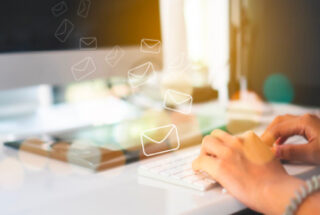 An image of a person's hands over a computer keyboard in front of a screen. There are envelope icons overlaying the image representing the sending of emails.