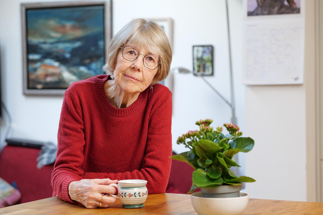 Helen Kendall in her kitchen, wearing a red jumper and holding a cup of tea, looking at the camera.