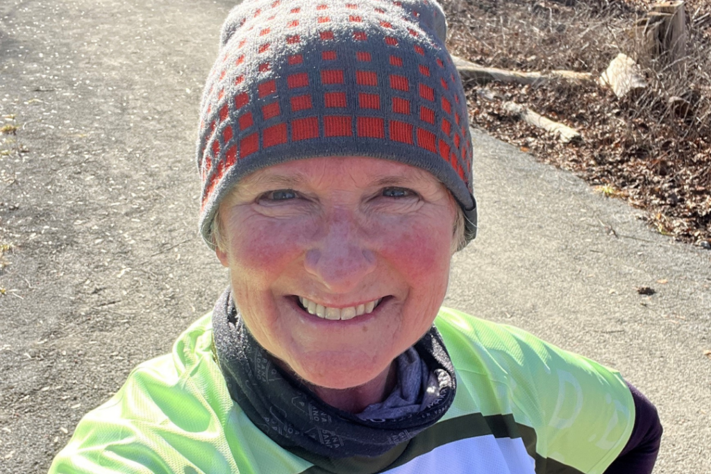 Deborah smiling to the camera on a training run, wearing a hat and an RNID running tshirt.