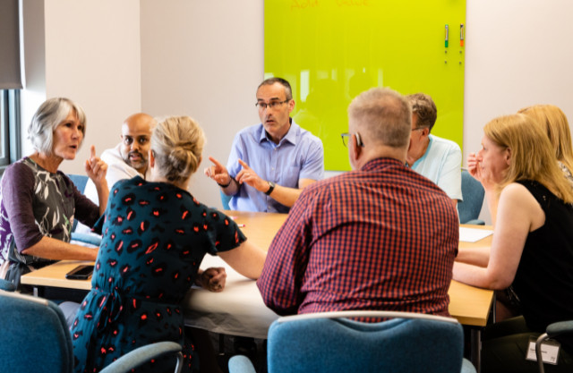 A group of work colleagues seated around a meeting room table, in discussion