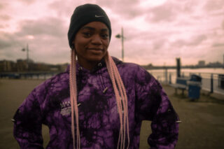 Sarah, a cochlear implant user, standing outside at dusk with hands on hips and smiling.