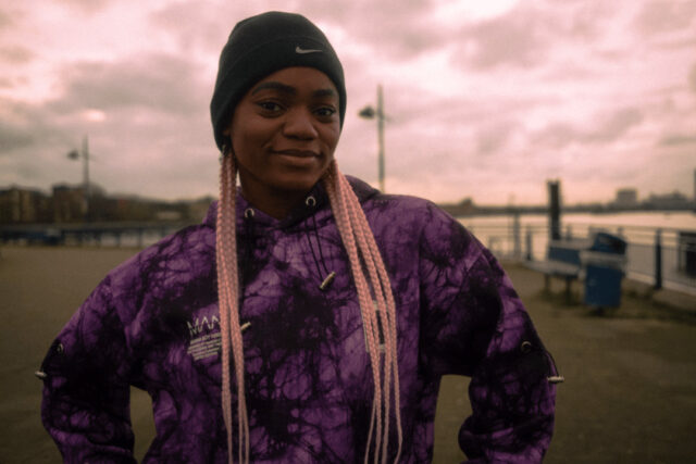 Sarah, a cochlear implant user, standing outside at dusk with hands on hips and smiling.