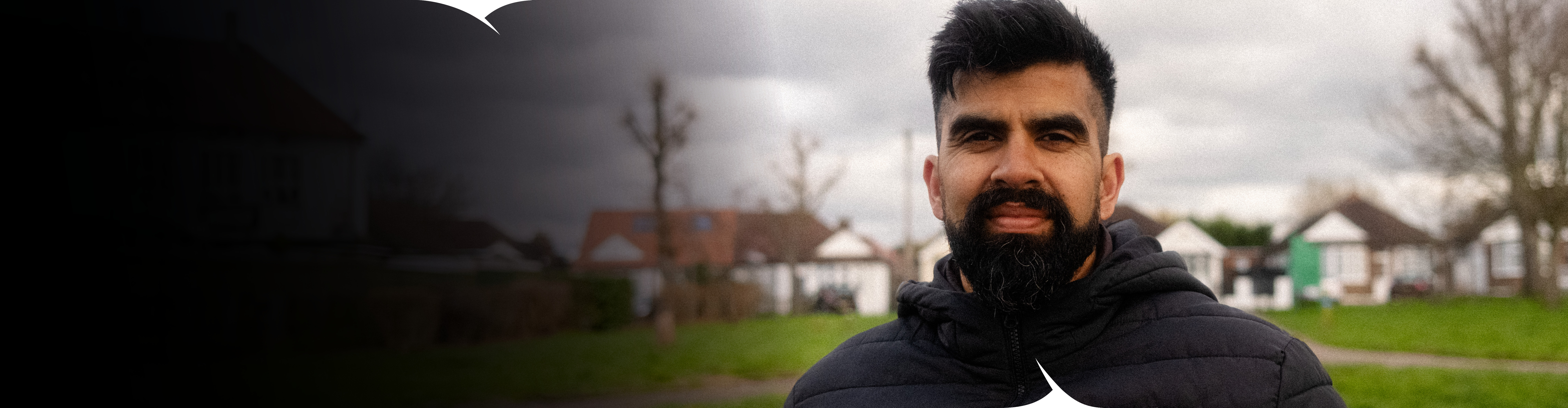 A man, standing in a park and smiling at the camera.