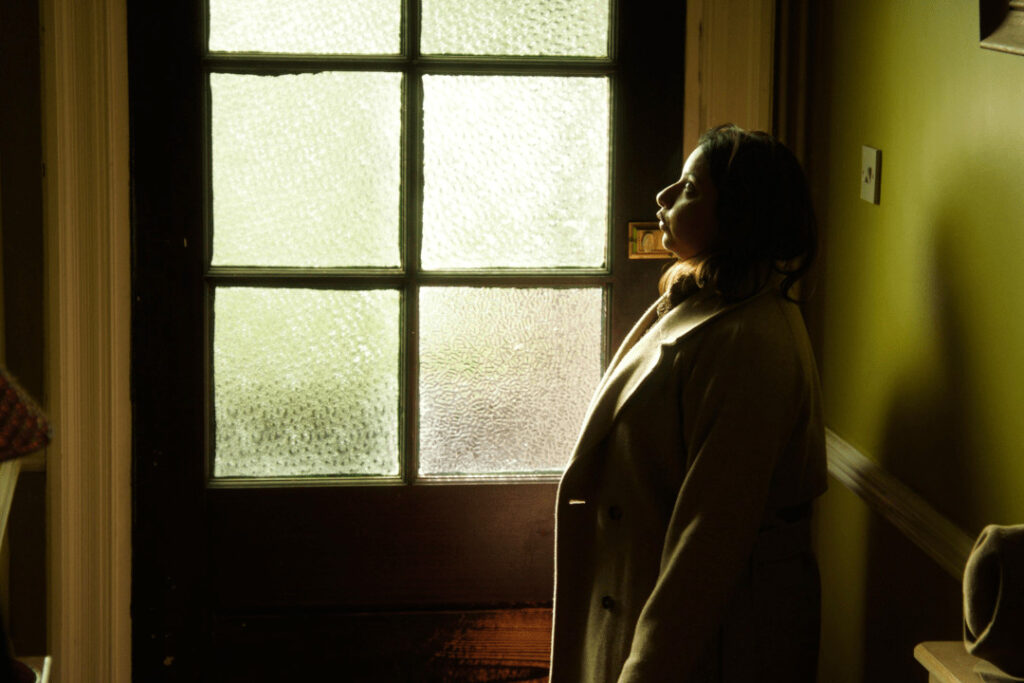 Kori stands in her hallway wearing her coat.