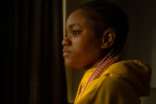 A young woman in a yellow hoodie gazing out the window, lost in thought.