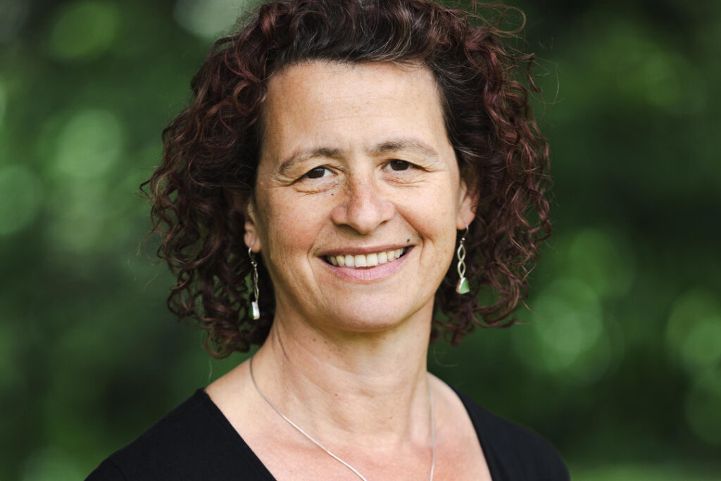 Harriet Oppenheimer, RNID's CEO. She stands outside in front of some green trees and smiles at the camera.