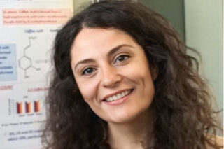 A photograph of Dr Fabiola Paciello. She stands in front of a science poster in a laboratory, smiling athe camera.