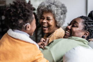 A family sit in a living room, laughing and smiling with each other. An older woman smiles at a boy who wears a hearing aid.