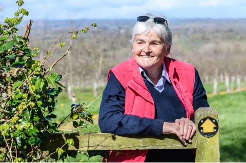 Sue Strachan, RNID Supporter and ARUK Ambassador, leaning on a fence in the countryside and smiling