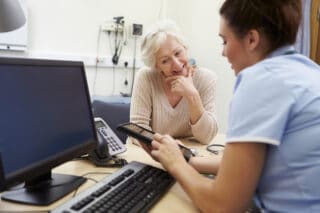 Healthcare professional at their desk, talking to a patient and looking at a handheld device