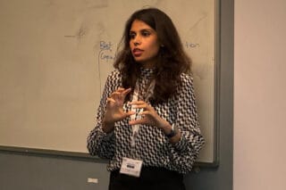 Oneeba Ahmed stands in a room giving a presentation