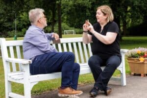 Two people sitting together on a park bench signing with each other.