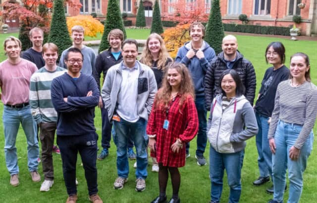 A photograph of University of Sheffield's hearing researchers. They stand outside on the grass on the university campus, smiling the camera.