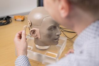 An RNID researcher working with a model head and prototype hearing device.