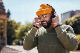 A man smiling wearing a woollen hat and headphones - graphics depicting soundwaves are coming from the headphones.