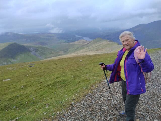 An older woman waves during a hike on Snowdon.