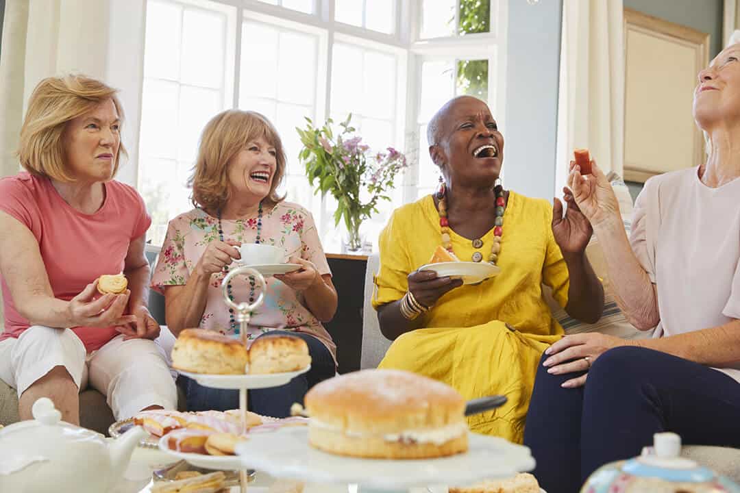 A group of people seated around a table enjoying tea and cake.