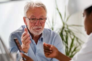 A patient in a hospital discussing treatment with his doctor who is looking at a handheld device.