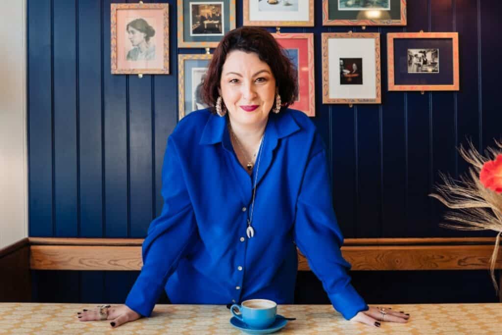 Actor, comedian and author, Samantha Baines standing at a table with a cup of coffee