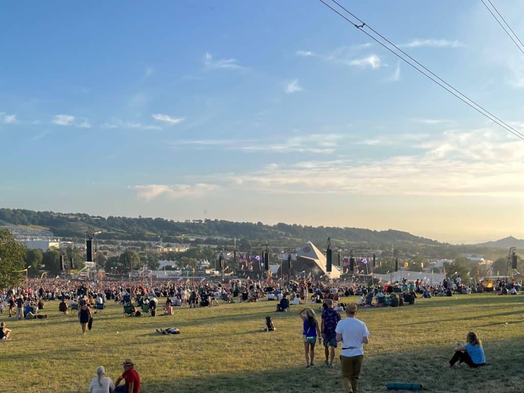 View from the back of the field at Glastonbury Festival, with crowds gathered in front of the Pyramid Stage as the sun sets behind it.