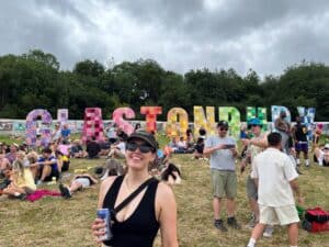 Franki Oliver, RNID Audiology Manager, smiling in front of the brightly coloured Glastonbury sign on a sunny day.