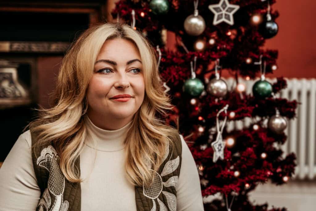 A woman with brown hair with blonde streaks sitting in front of a Christmas tree.