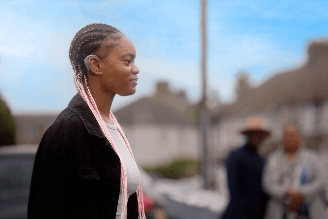 Young woman with hearing aid outdoors, representing hearing loss awareness and support.
