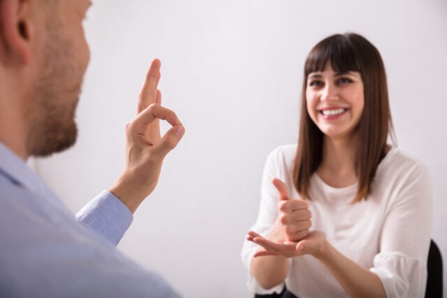 A woman facing a man. They communicate in sign language.