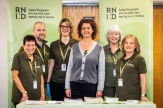 RNID Near You volunteers and RNID CEO, Harriet Oppenheimer, stand in front of green RNID banners.
