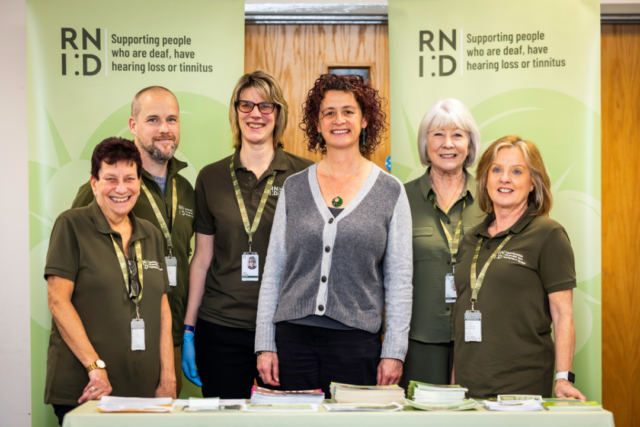 RNID Near You volunteers and RNID CEO, Harriet Oppenheimer, stand in front of green RNID banners.