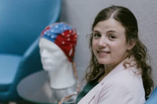 A scientist with brown hair wears a lab coat and smiles.