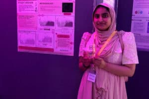 Student Farzana stands at an event holding an award.