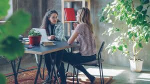 Two women seated at a table in an office, one has a laptop