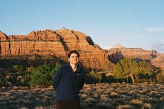 A man stands in front of a mountain dessert scene.