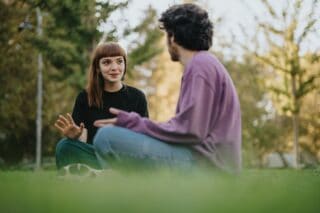 A woman and a man sitting outside on the grass using sign language