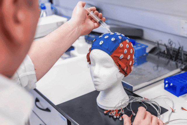 Photo of tinnitus researchers at Newcastle University in a lab, holding a syringe above a cap on a polystyrene head as part of an experimental setup.